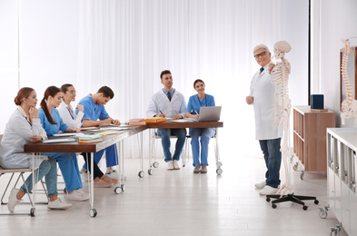 Medical students and professor studying human skeleton anatomy in classroom