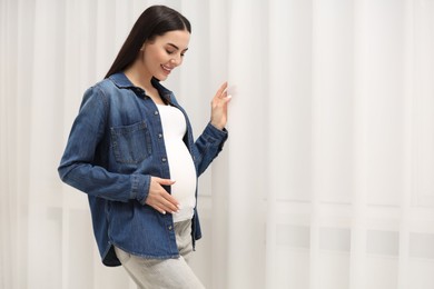 Photo of Happy pregnant woman near window indoors, space for text