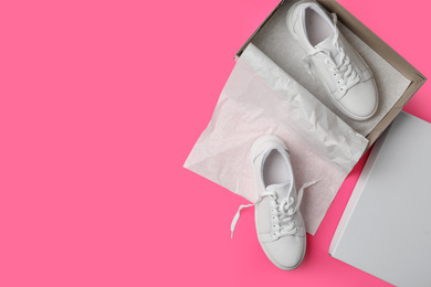 Photo of Stylish white shoes and cardboard box on pink background, flat lay. Space for text