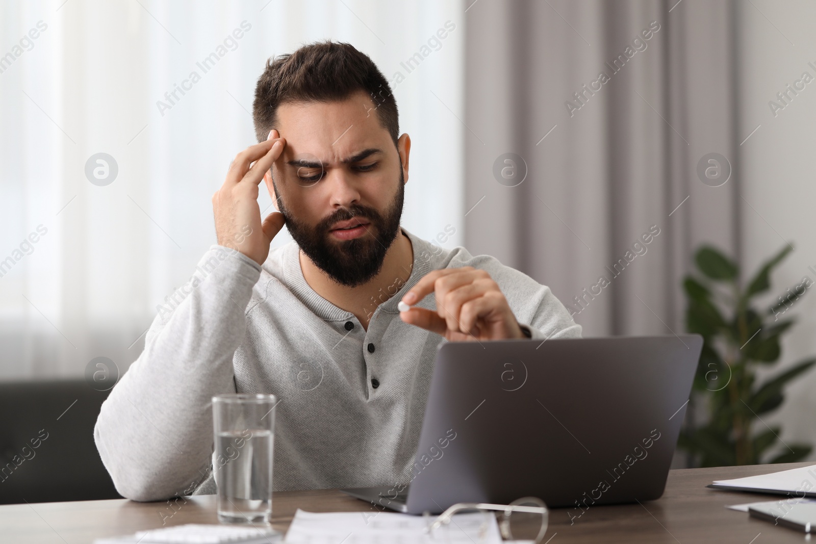 Photo of Man with pill suffering from headache at workplace in office