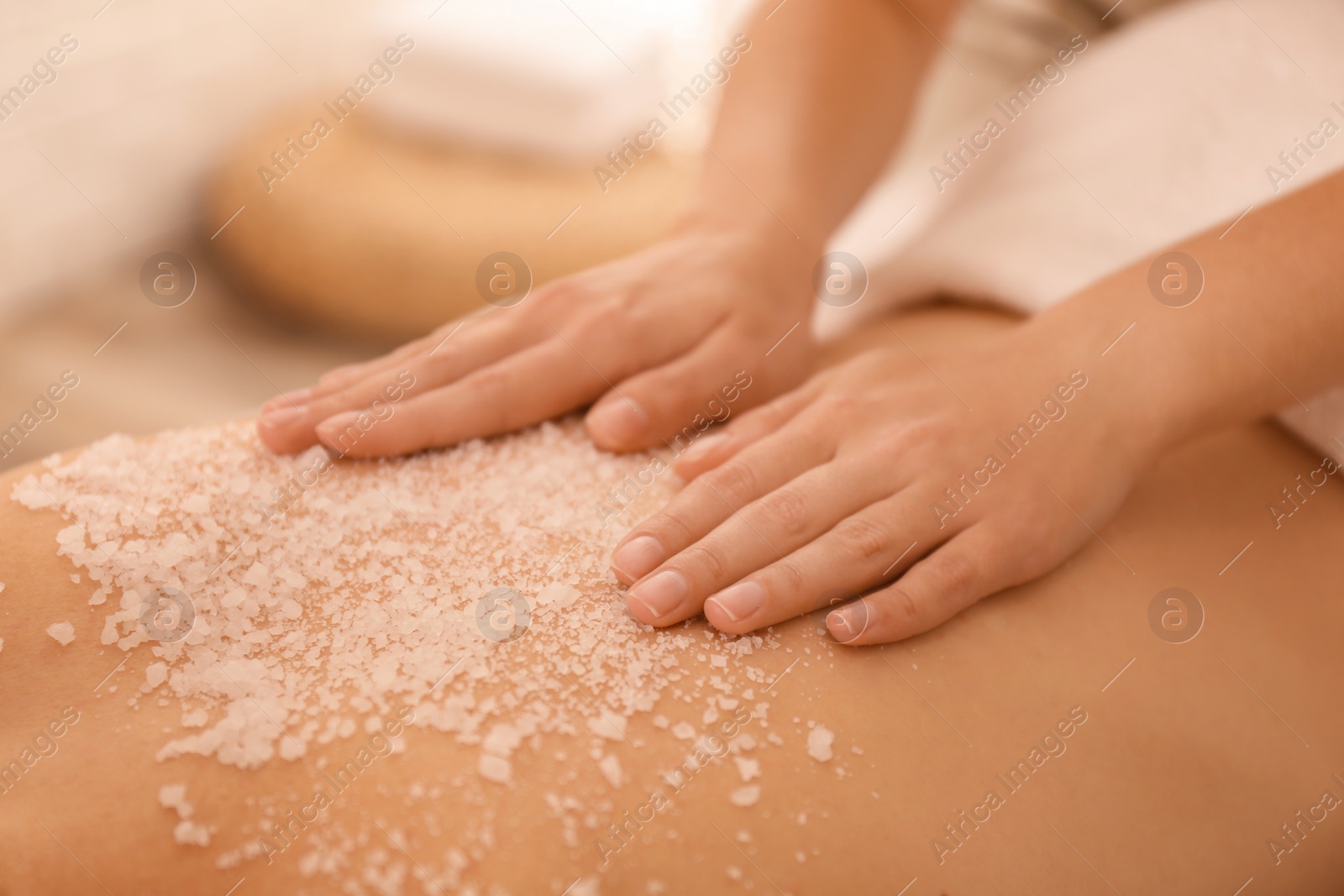 Photo of Young woman having body scrubbing procedure with sea salt in spa salon, closeup