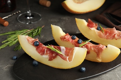 Photo of Melon with prosciutto, blueberries and rosemary on grey table