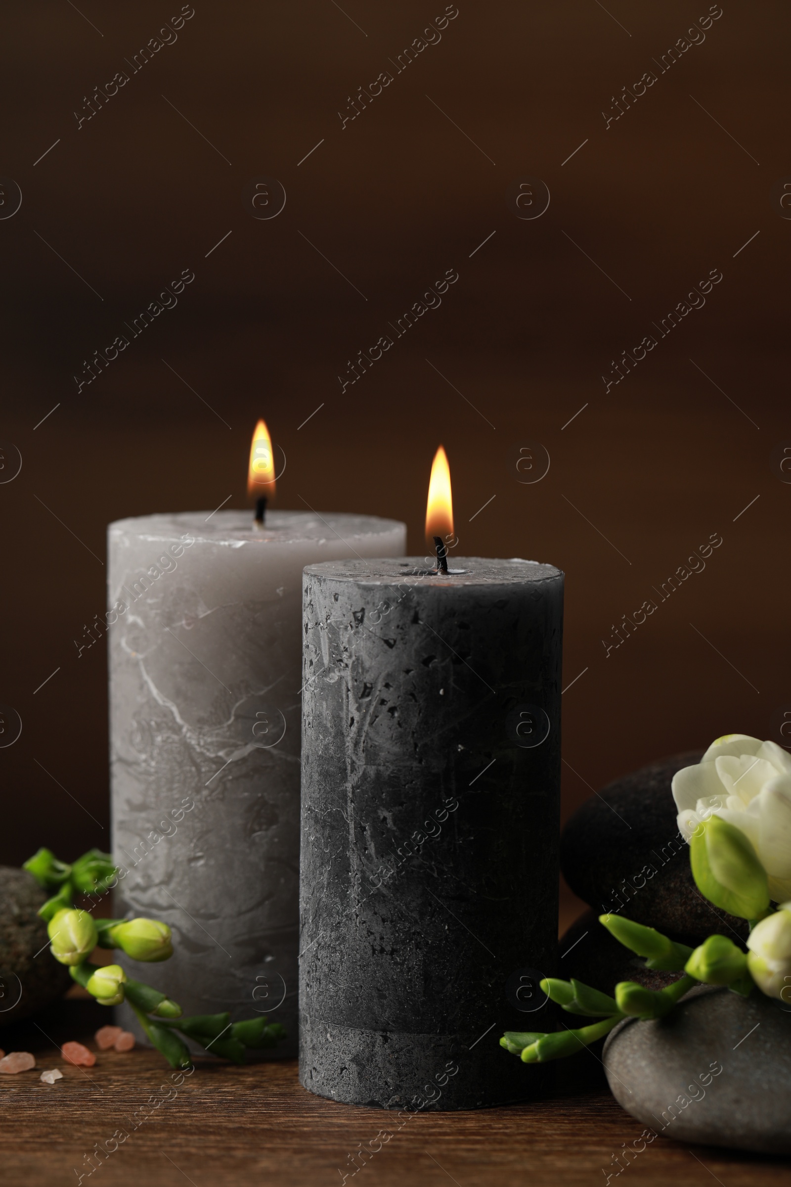 Photo of Beautiful composition with burning candles, spa stones and flowers on wooden table