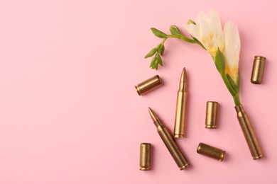Photo of Bullets and cartridge cases with beautiful flower on pink background, flat lay. Space for text