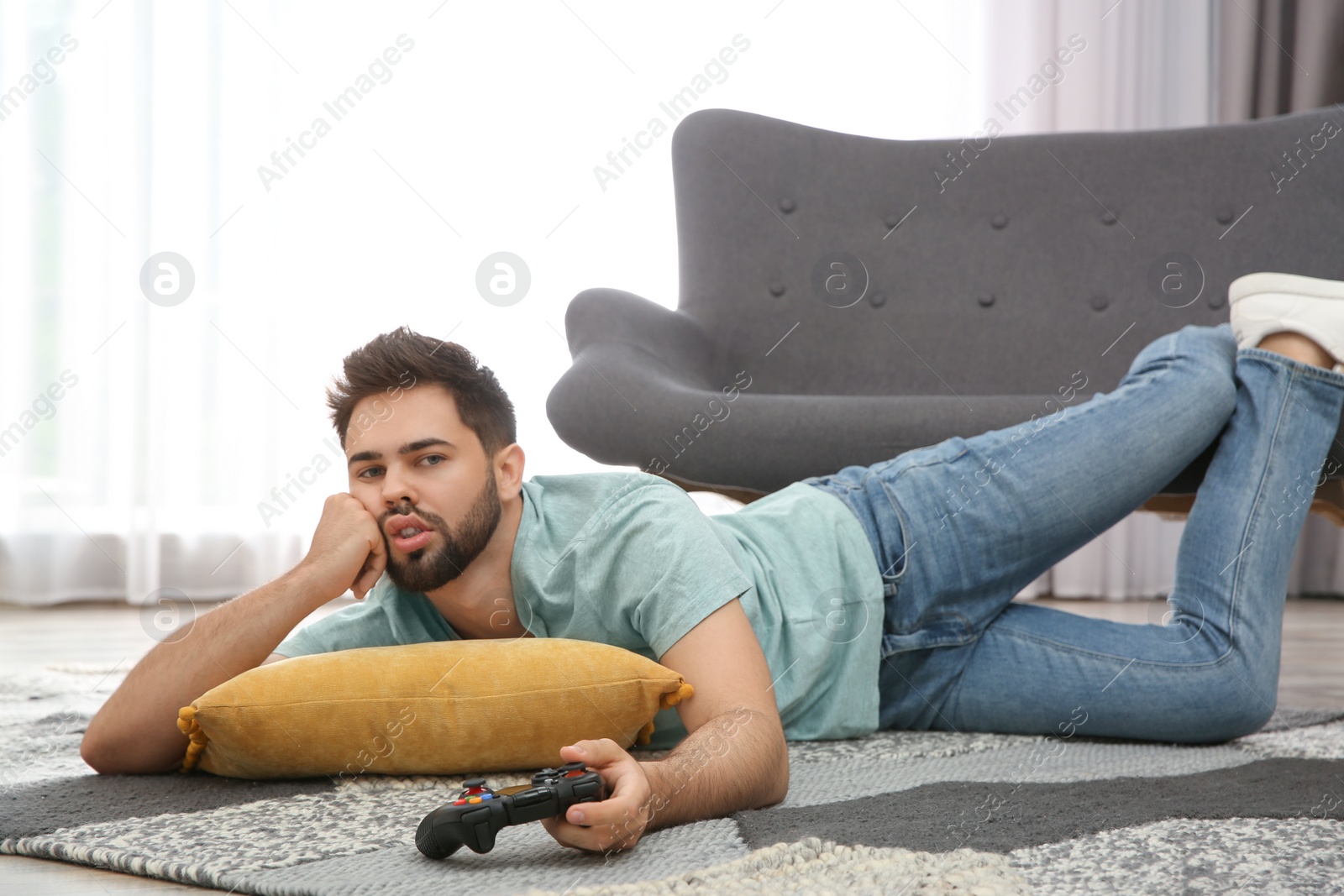 Photo of Lazy young man playing video game while lying on floor at home