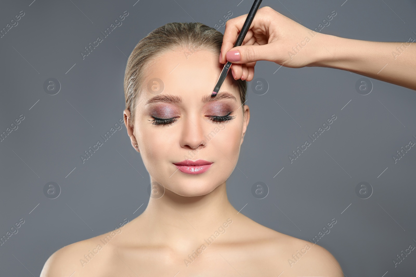 Photo of Artist applying makeup onto woman's face on light grey background