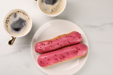 Photo of Tasty glazed eclairs and cups of coffee on white marble table, flat lay