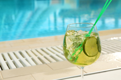 Photo of Glass of delicious mojito near swimming pool, space for text. Refreshing drink
