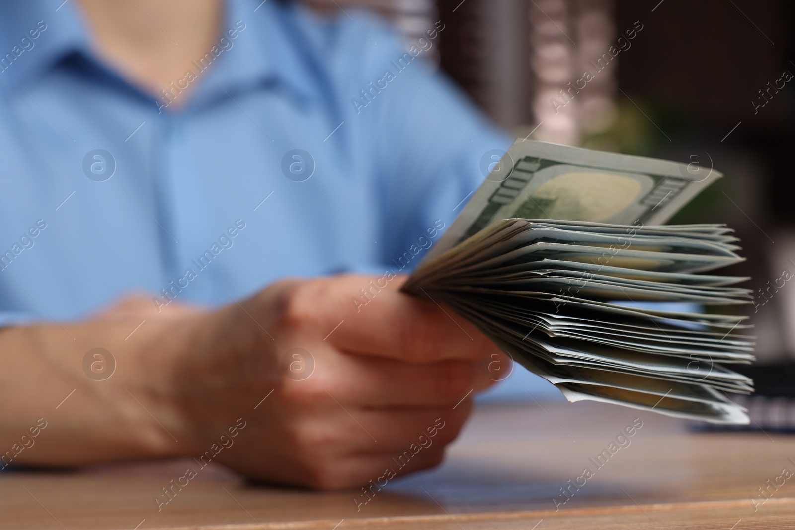 Photo of Money exchange. Woman holding dollar banknotes at wooden table, closeup