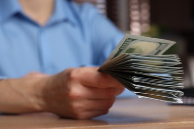 Photo of Money exchange. Woman holding dollar banknotes at wooden table, closeup