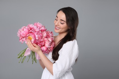 Beautiful young woman with bouquet of pink peonies on grey background