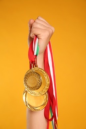 Photo of Woman holding gold medals on yellow background, closeup