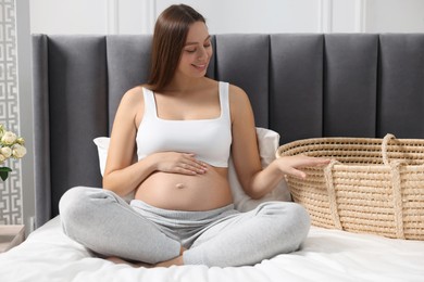 Beautiful pregnant woman with baby basket on bed indoors