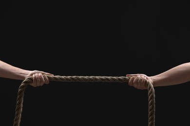 Photo of Dispute concept. Men pulling rope on black background, closeup. Space for text