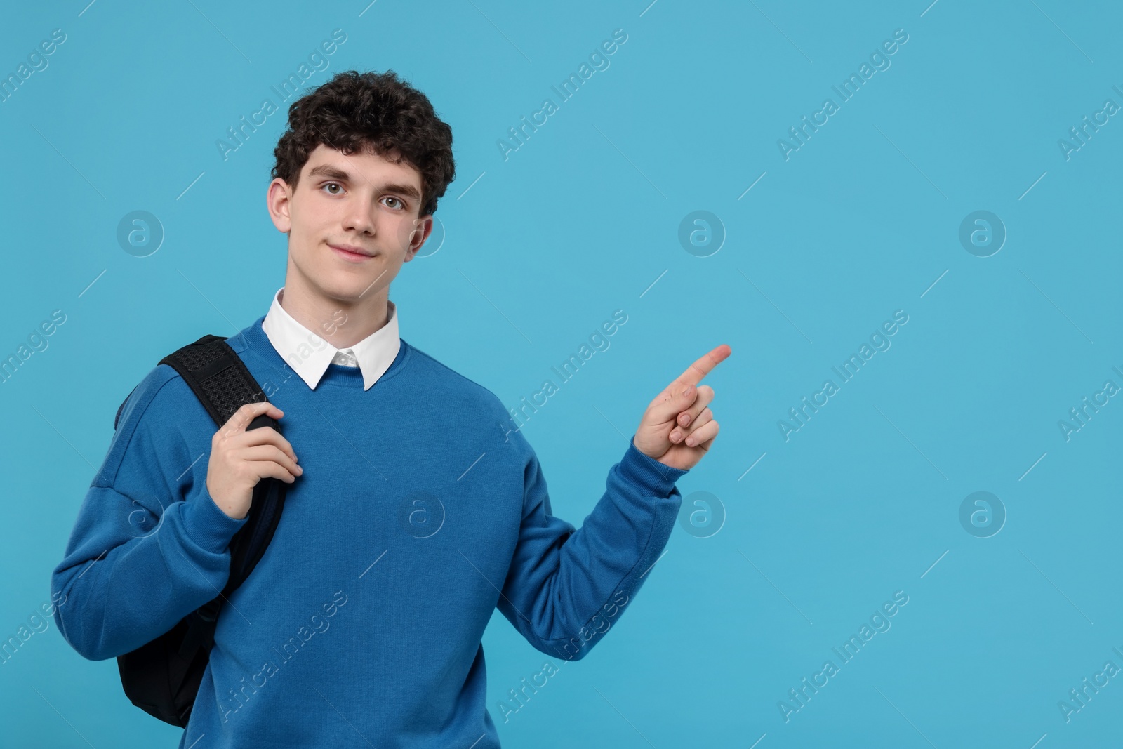 Photo of Portrait of student with backpack pointing on light blue background. Space for text