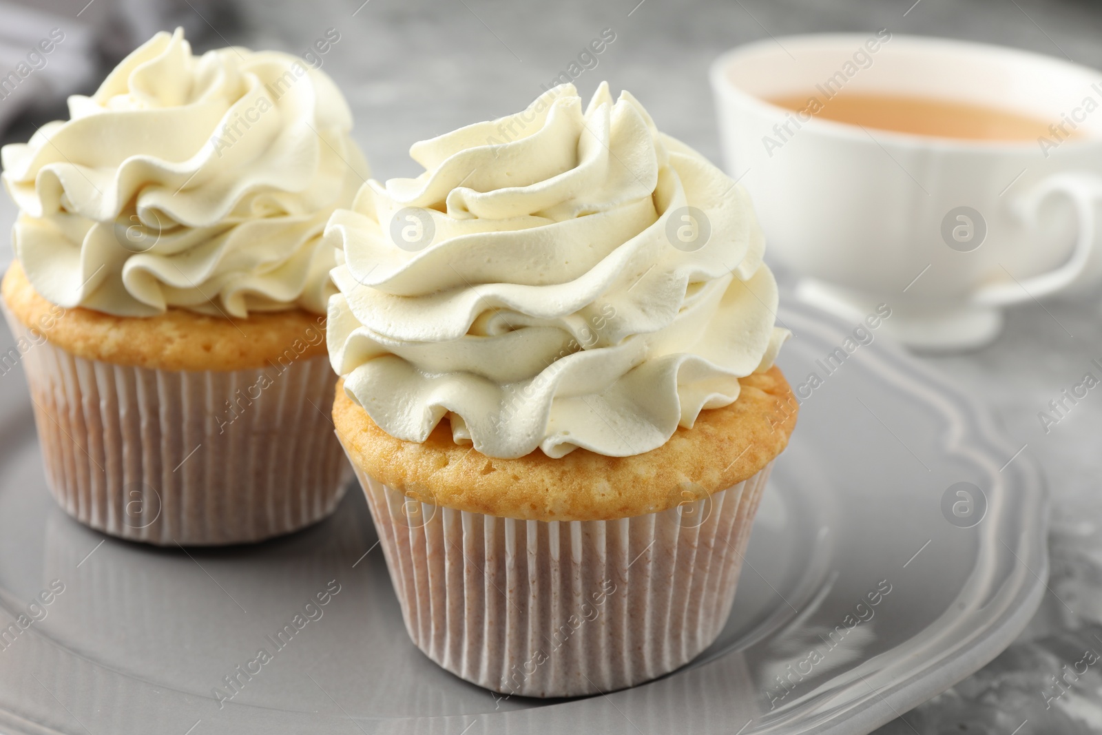 Photo of Tasty cupcakes with vanilla cream on grey table, closeup