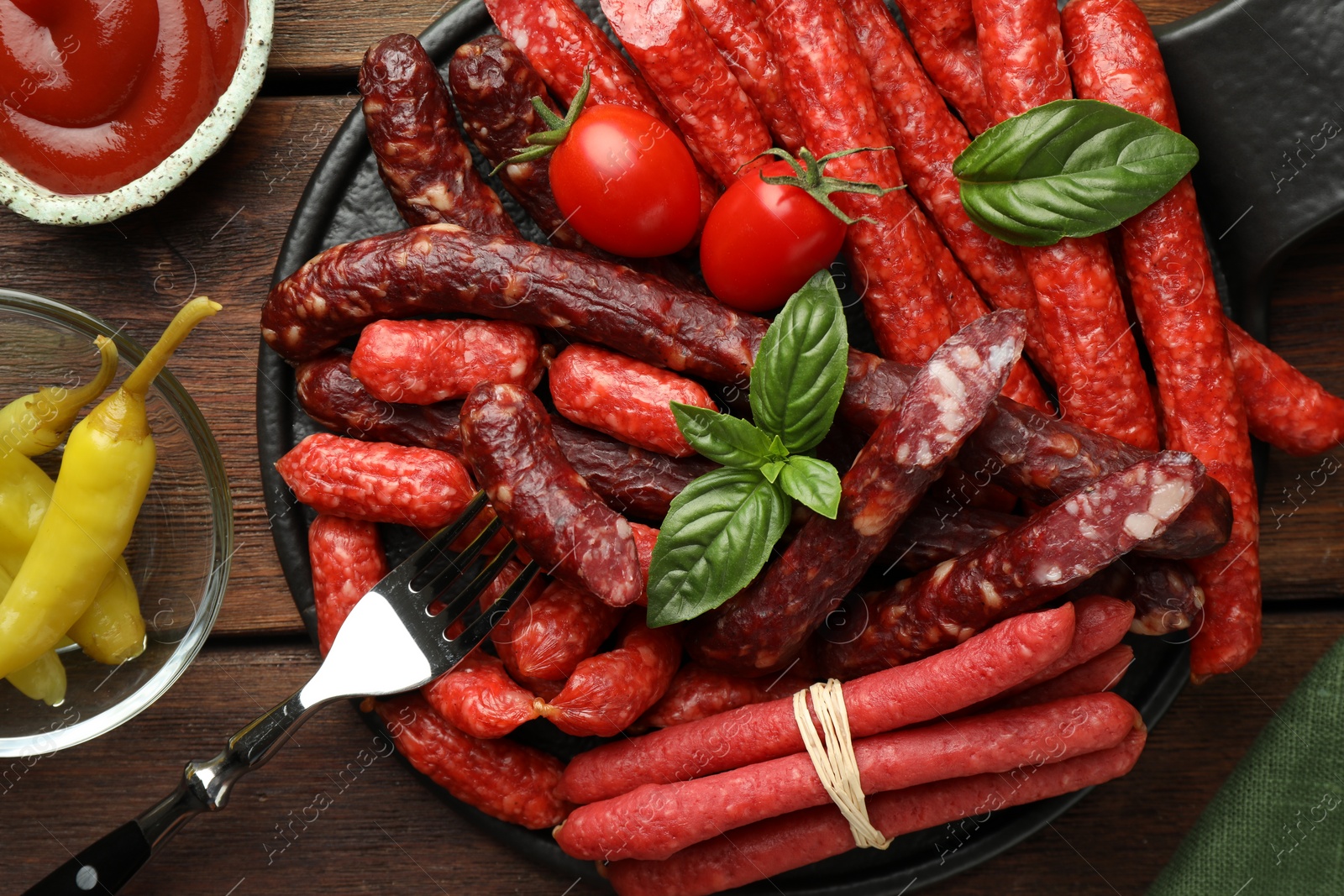 Photo of Different thin dry smoked sausages, sauce and tomatoes on wooden table, flat lay