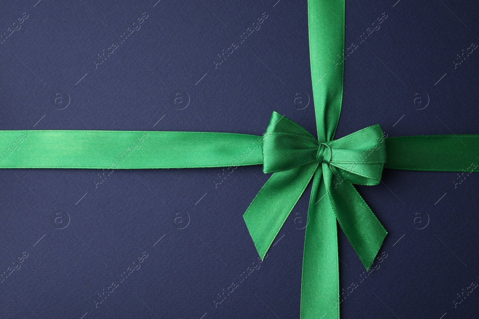 Photo of Green satin ribbon with bow on blue background, top view