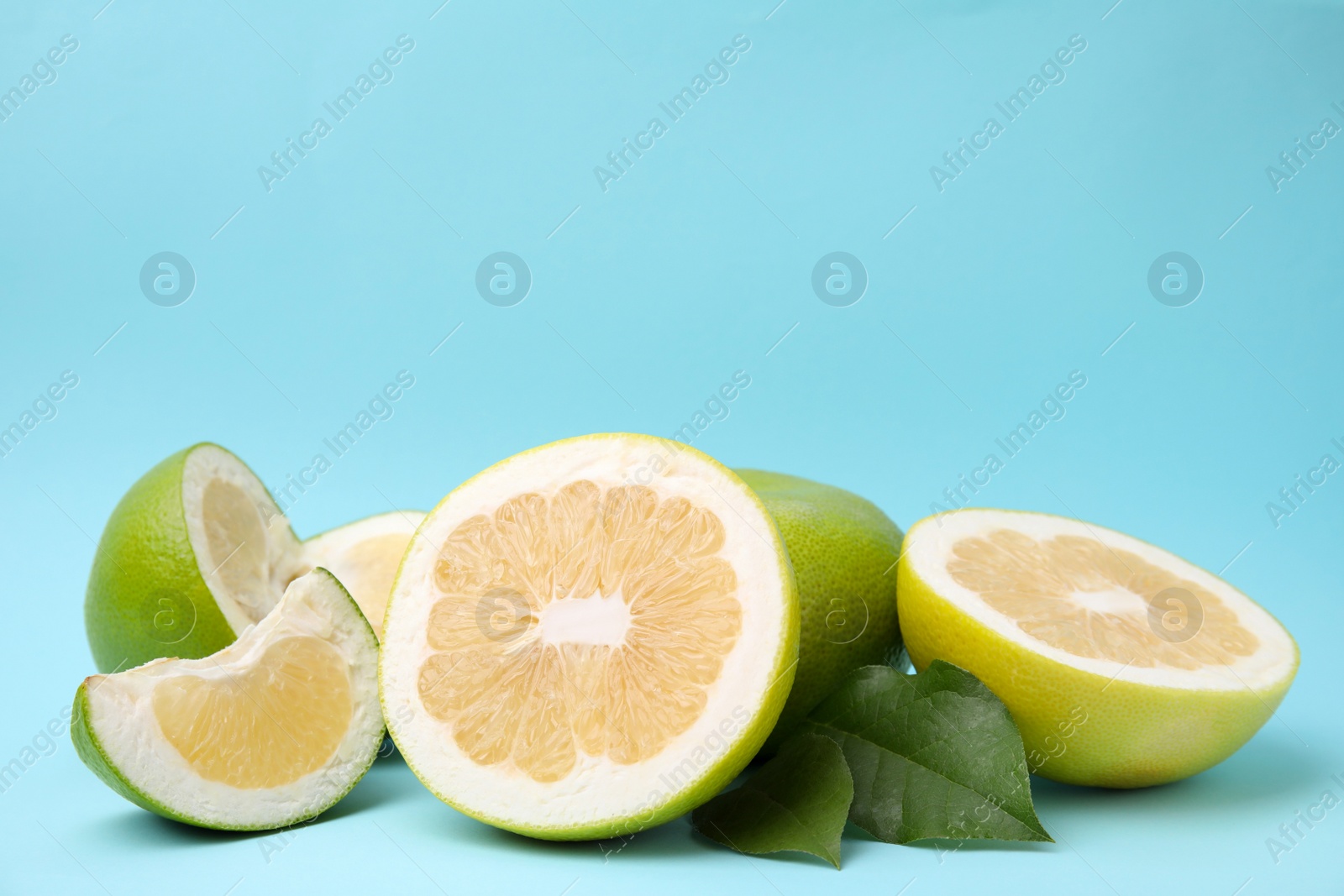 Photo of Whole and cut sweetie fruits with green leaves on light blue background. Space for text