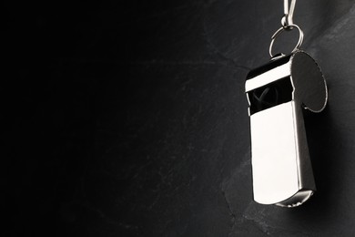 Referee equipment. Metal whistle on black textured background, closeup and space for text