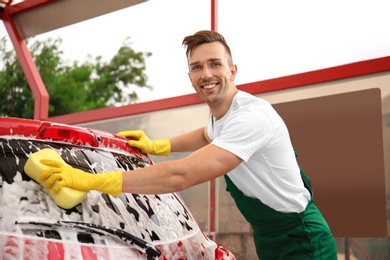 Male worker cleaning vehicle with sponge at car wash