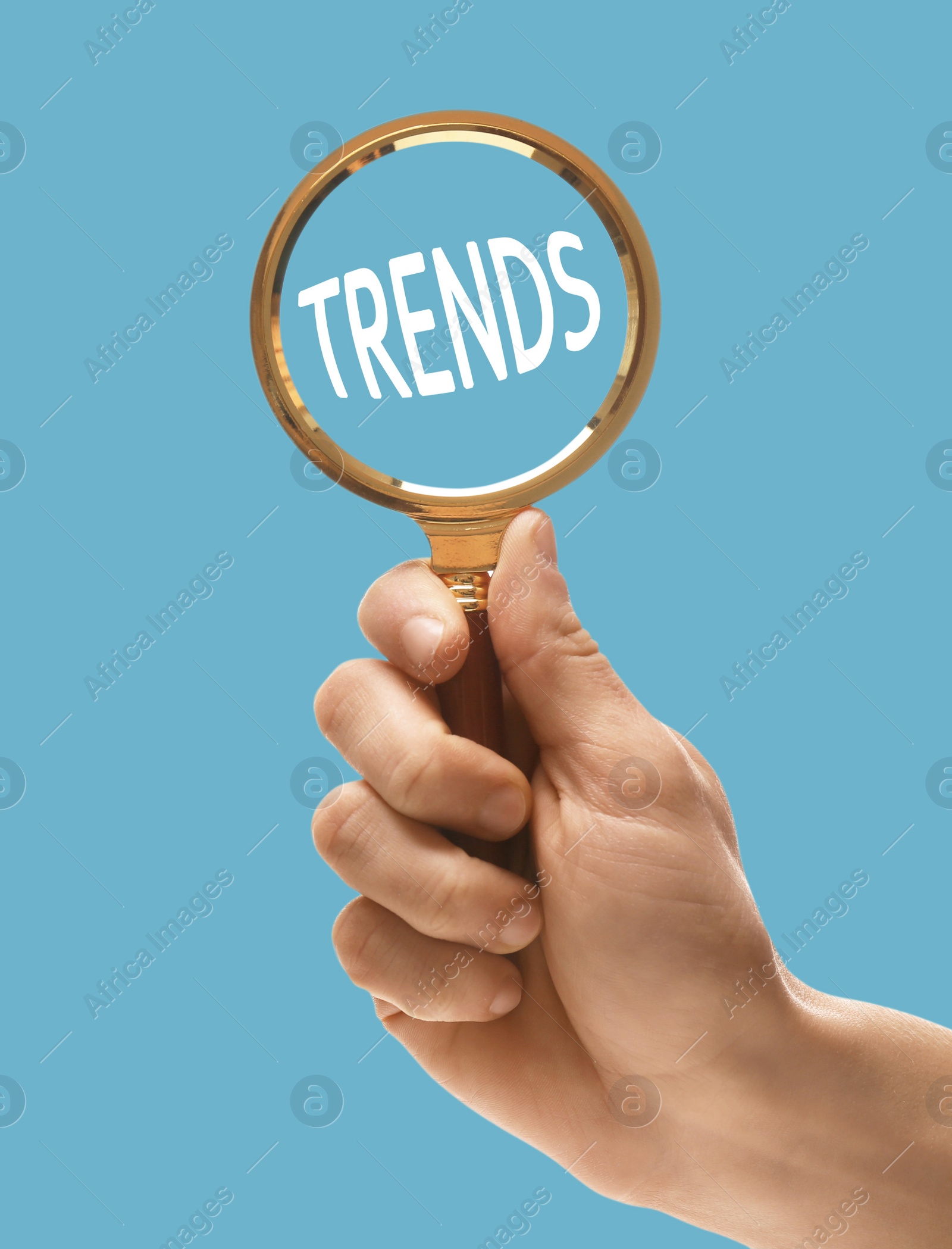 Image of Searching new and popular trends. Woman holding magnifying glass over word on light blue background, closeup