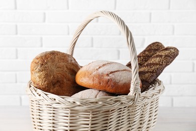 Photo of Different types of bread in wicker basket on table against white brick wall, closeup