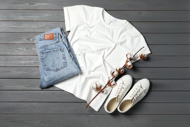 Stylish t-shirt, jeans and sneakers on grey wooden background, flat lay