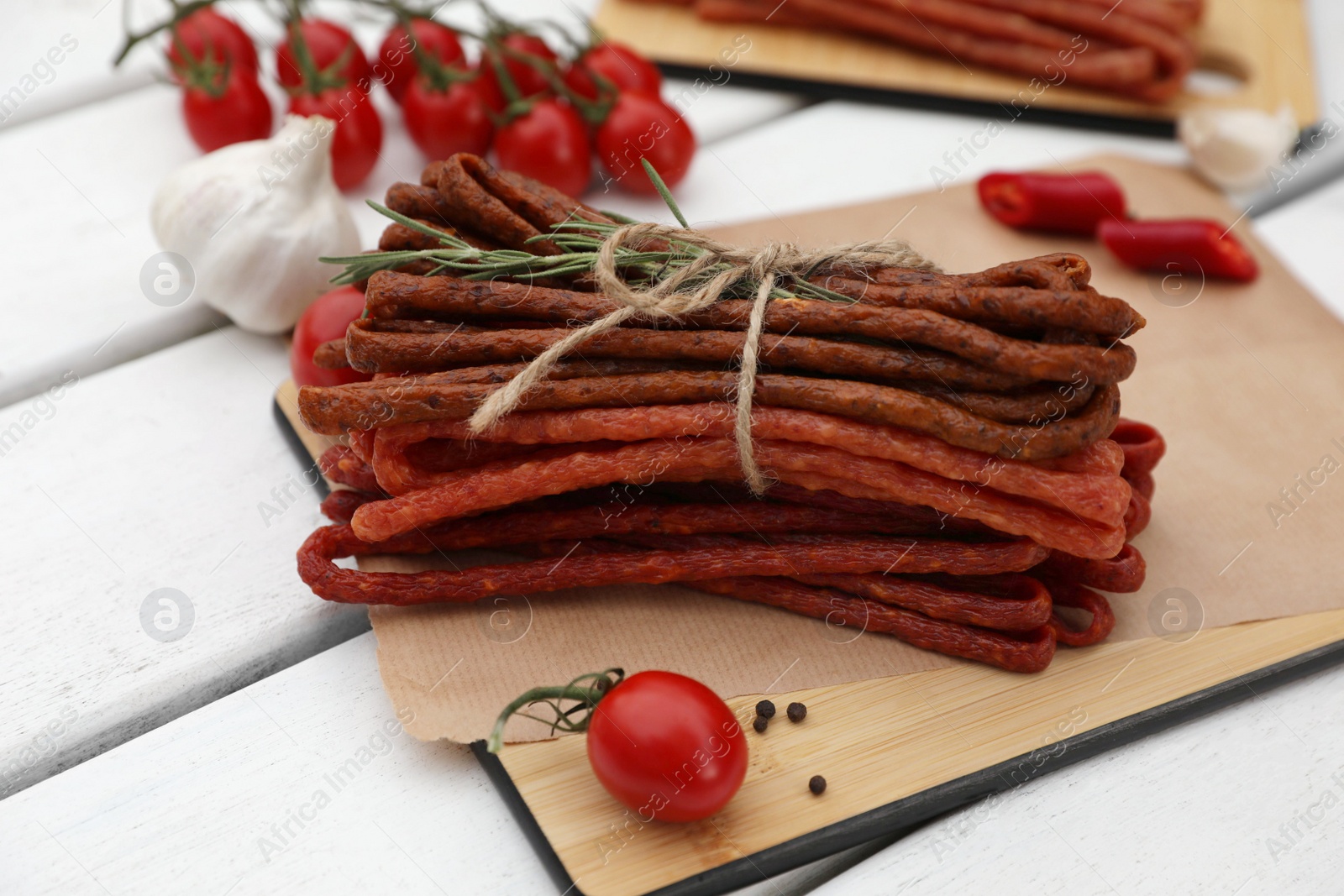 Photo of Delicious kabanosy with rosemary, peppercorn, chilli and tomatoes on white wooden table