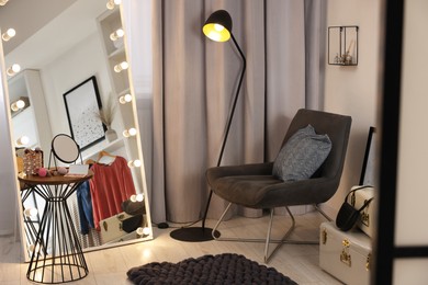 Photo of Makeup room. Stylish mirror with light bulbs, beauty products on table and armchair indoors