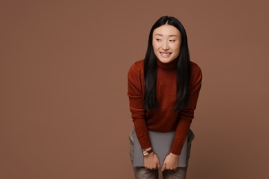 Portrait of smiling woman with laptop on brown background. Space for text