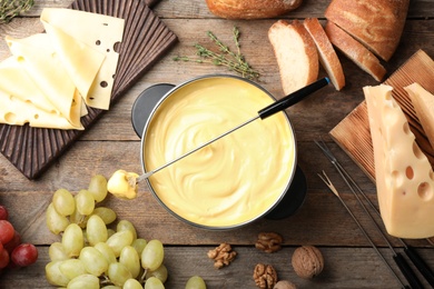 Photo of Flat lay composition with pot of delicious cheese fondue on wooden table