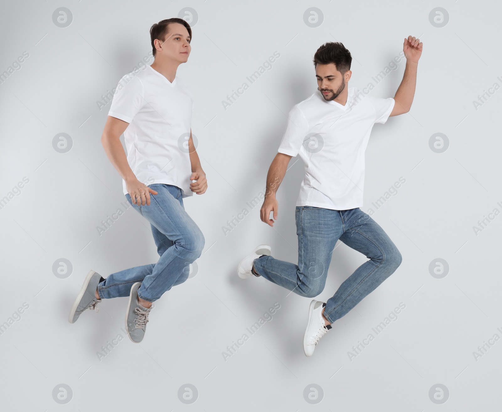 Photo of Young men in stylish jeans jumping on light background