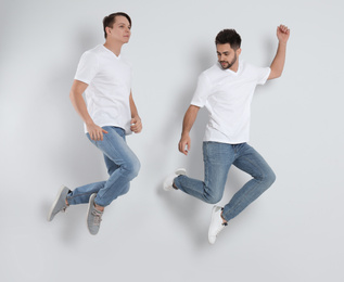 Young men in stylish jeans jumping on light background