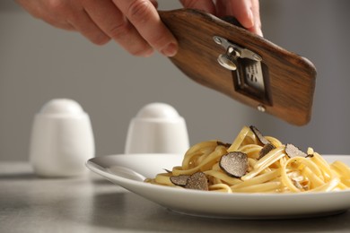 Photo of Woman slicing truffle onto fettuccine at grey table, closeup