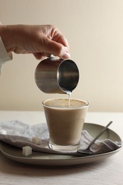 Photo of Pouring milk into cup with coffee on white wooden table, closeup