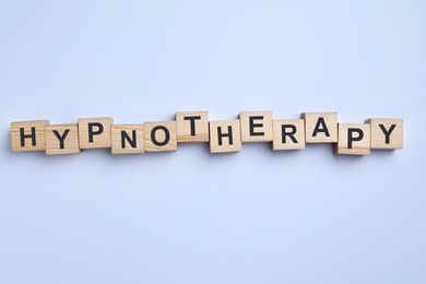 Photo of Wooden blocks with word HYPNOTHERAPY on white background, top view