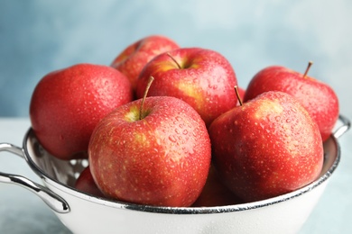 Photo of Colander with ripe juicy red apples on table against blue background, closeup