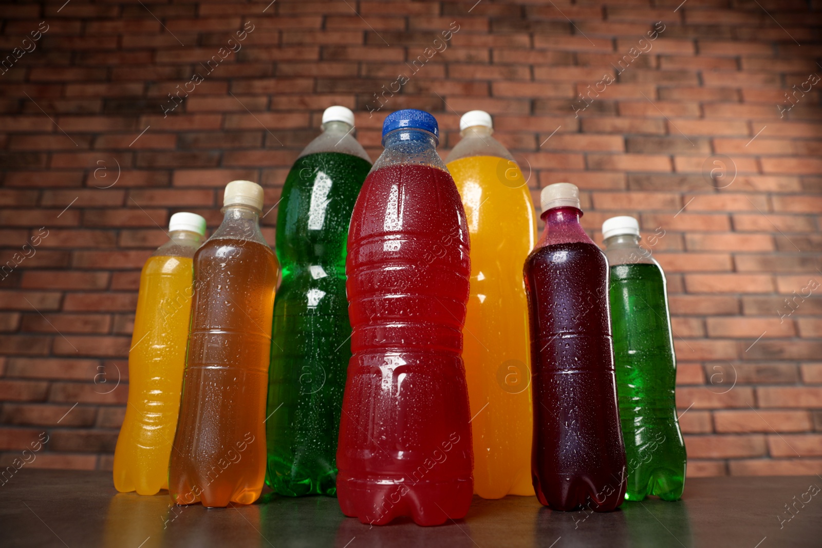 Photo of Bottles of soft drinks with water drops on table against brick wall, low angle view