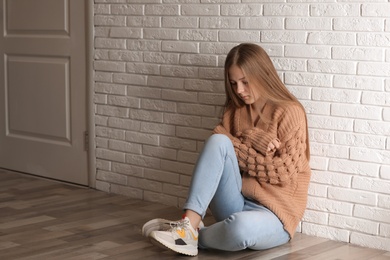 Photo of Upset teenage girl sitting alone on floor near wall