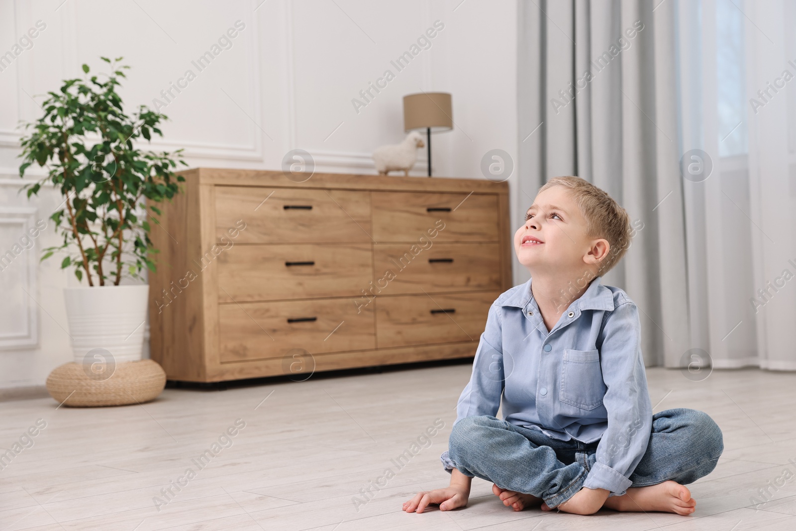 Photo of Cute little boy sitting on warm floor at home, space for text. Heating system