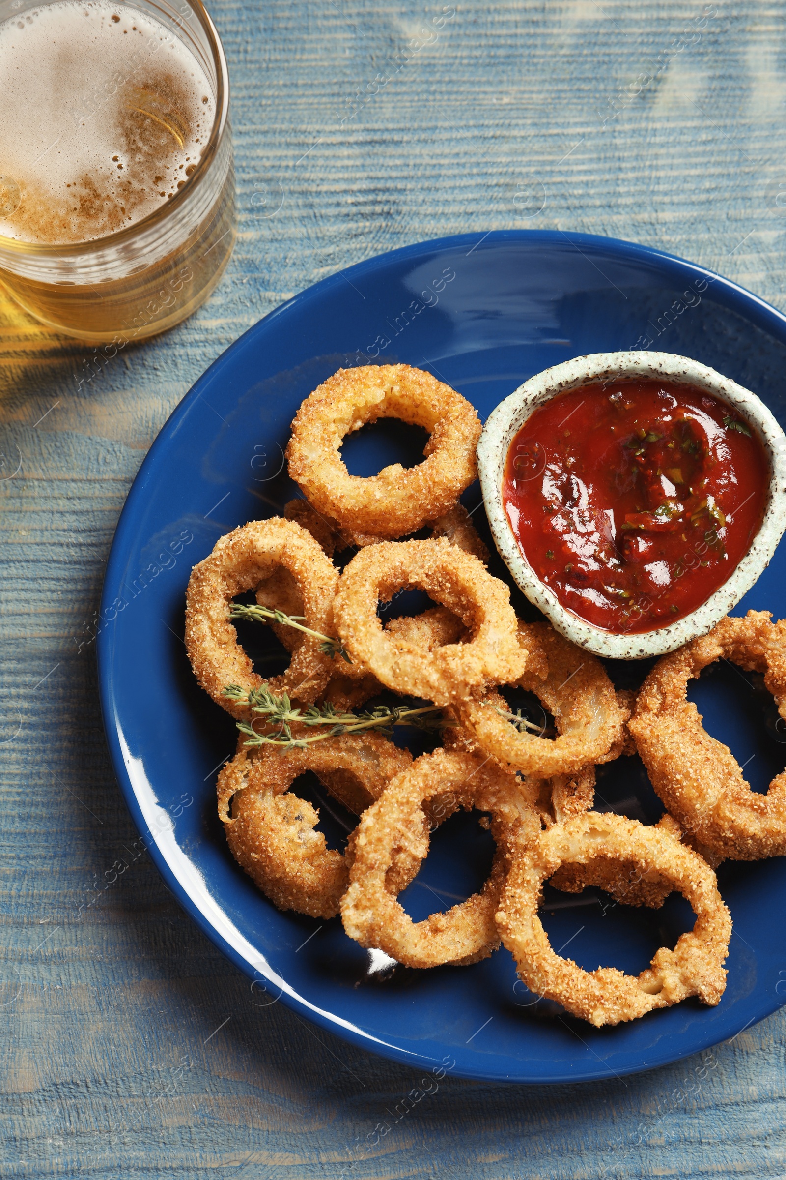 Photo of Plate with homemade crunchy fried onion rings and tomato sauce on wooden background, top view