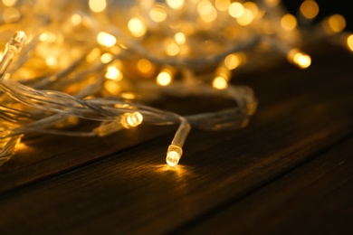 Photo of Glowing Christmas lights on wooden table, closeup view