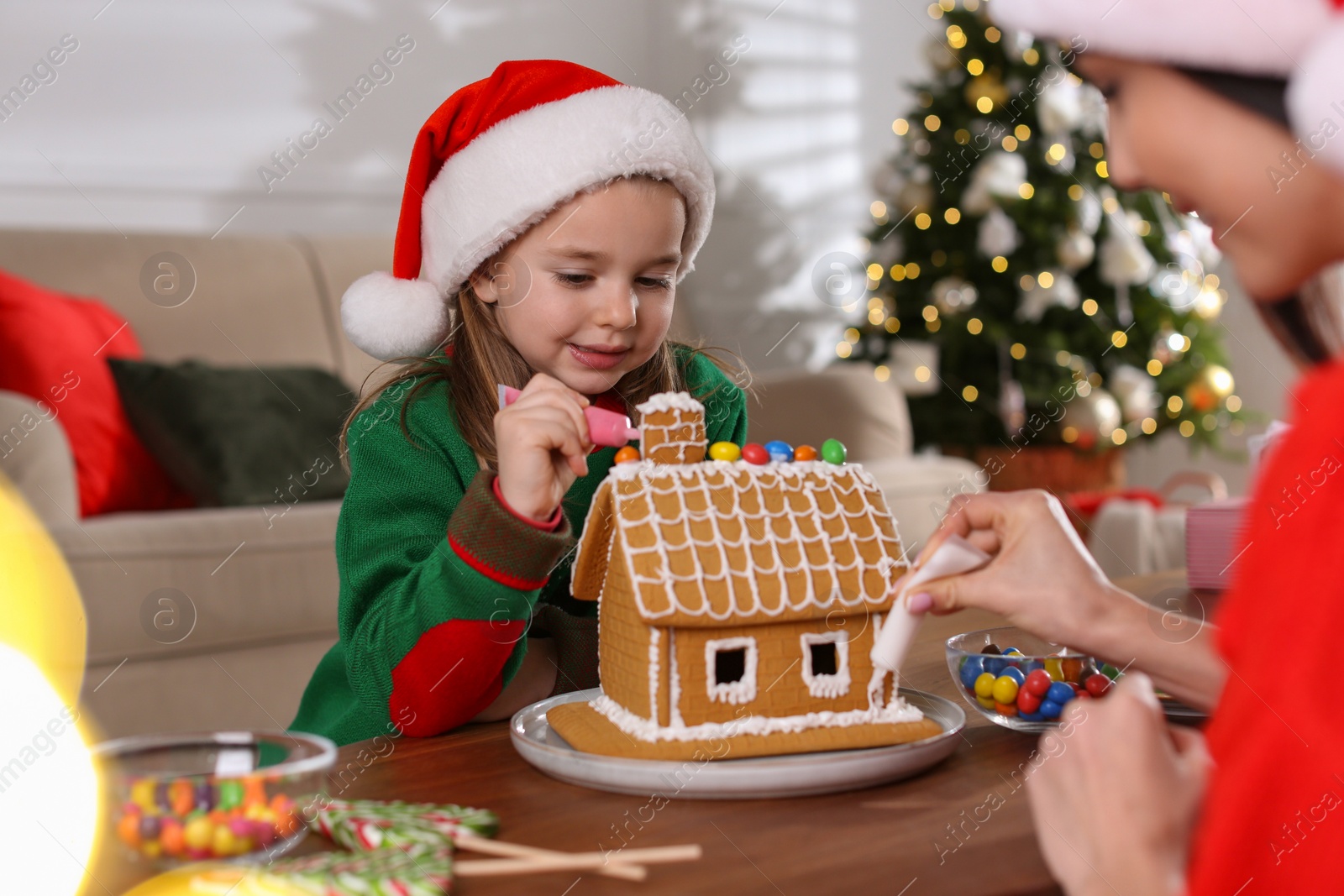 Photo of Mother and daughter decorating gingerbread house at table indoors