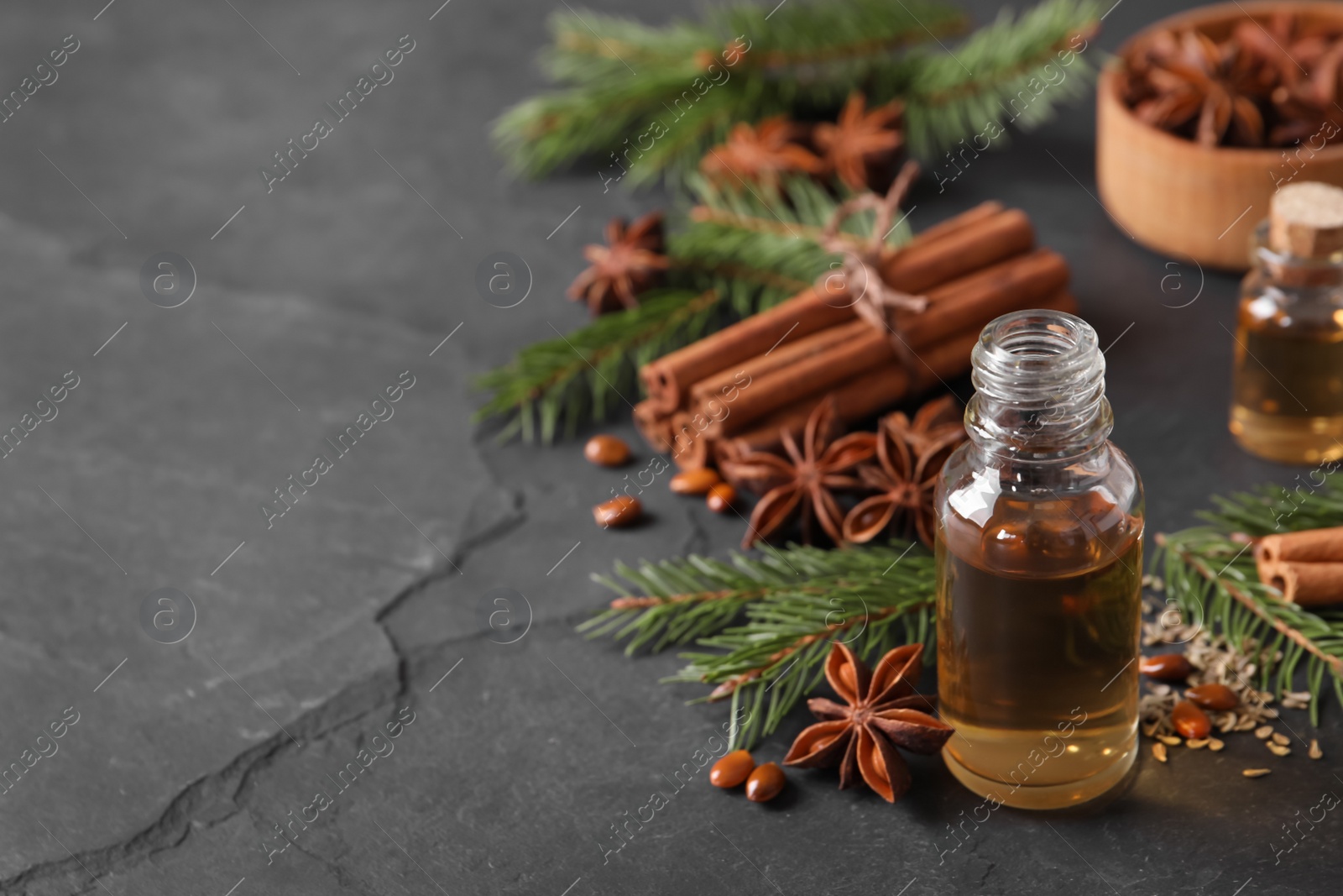 Photo of Bottle of essential oil, anise, cinnamon and fir tree branches on black table. Space for text