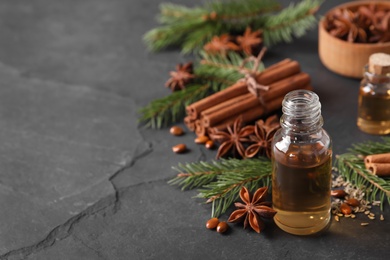 Bottle of essential oil, anise, cinnamon and fir tree branches on black table. Space for text