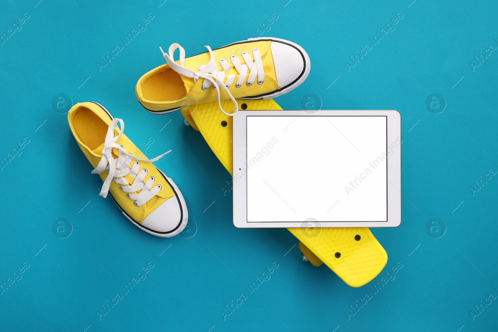 Photo of Modern tablet, skateboard and shoes on light blue background, flat lay. Space for text