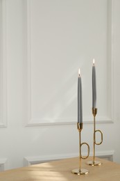 Photo of Holders with burning candles on wooden table near white wall indoors, space for text