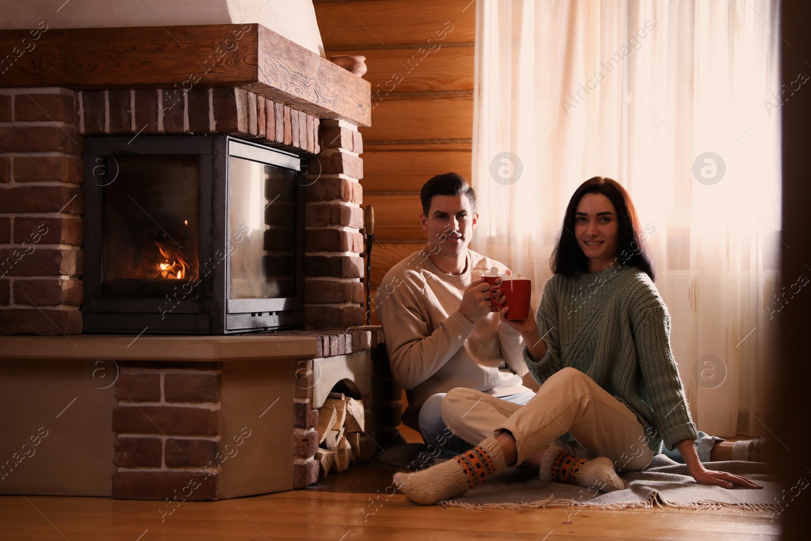 Photo of Lovely couple with delicious cocoa near fireplace on floor at home. Winter vacation