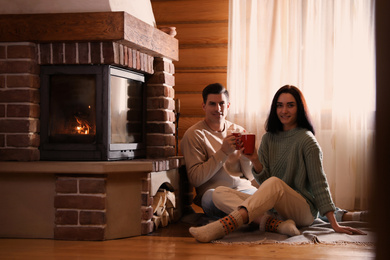 Photo of Lovely couple with delicious cocoa near fireplace on floor at home. Winter vacation
